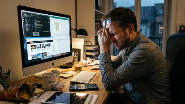 sin lograr concentrarse un señor frente a una pantalla de computadora con expresión de abrumado, superado por sus distraciones, un movil en la escena