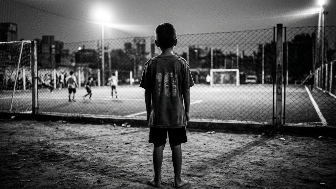 Origen del gen competitivo argentino Un niño de espaldas, con una camiseta de fútbol de potrero (desgastada), mirando hacia una cancha iluminada o un arco. Esto evoca la pasión, la infancia y el peso de la expectativa.